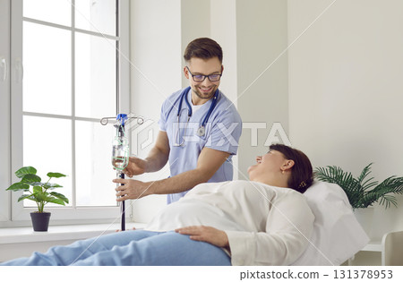 Nurse gives an IV line to a woman patient lying on the medical bed at the hospital 131378953