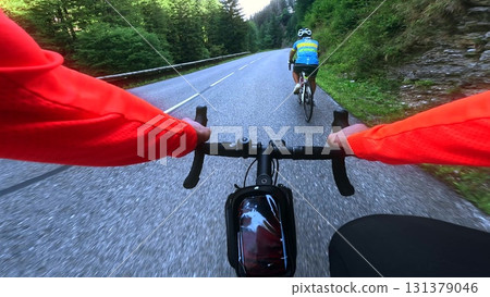 First-person view of a road cyclist overtaking another amateur rider on a winding mountain road in the Vercors, France. Action sports and outdoor cycling in alpine scenery First-person view of a road cyclist overtaking another amateur rider on a winding mountain road in the Vercors, France. Action sports and outdoor cycling in alpine scenery 131379046