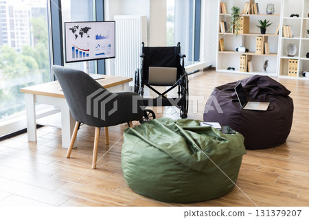 Bright office setup featuring wheelchairs, laptops on bean bags, large screen displaying graphs Bright office setup featuring wheelchairs, laptops on bean bags, large screen displaying graphs 131379207