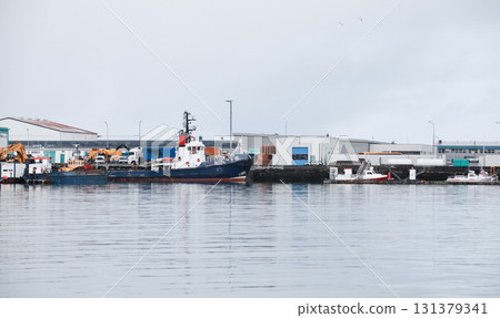 Industrial harbor along a quay shows a large blue ship, cranes, and warehouses 131379341