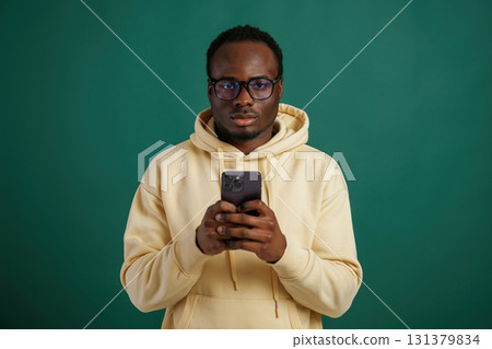 Using smartphone. African American man is standing against green background in the studio 131379834