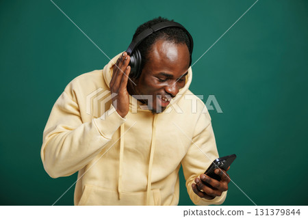 In headphones, enjoying music. African American man is standing against green background in the studio In headphones, enjoying music. African American man is standing against green background in the studio 131379844