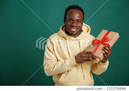 Holding gift box. African American man is standing against green background in the studio Holding gift box. African American man is standing against green background in the studio 131379846