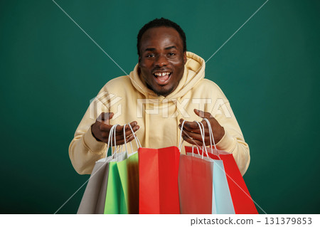 Shopping bags in hands, happy. African American man is standing against green background in the studio Shopping bags in hands, happy. African American man is standing against green background in the studio 131379853