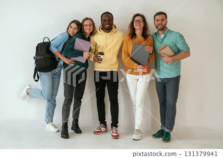 Smiling, looking forward. Group of young people are standing against white background Smiling, looking forward. Group of young people are standing against white background 131379941