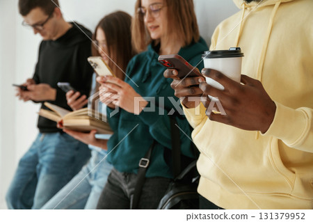 Busy by using smartphones. Group of young people are standing against white background Busy by using smartphones. Group of young people are standing against white background 131379952