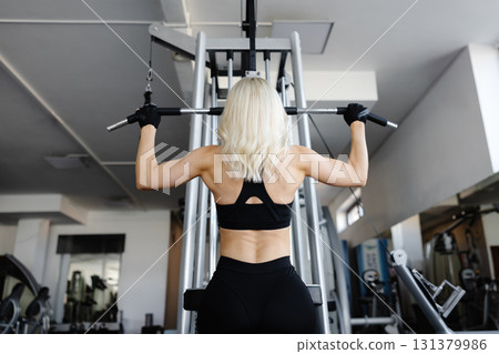 Athletic woman exercising back muscles using lat machine in gym 131379986