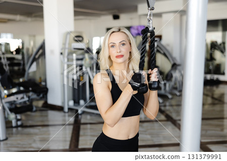 Determined sportswoman exercising back muscles using cable machine in gym Determined sportswoman exercising back muscles using cable machine in gym 131379991