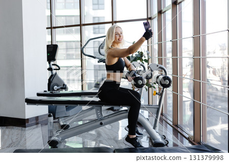 Athletic woman resting on bench after exercising with dumbbells in gym Athletic woman resting on bench after exercising with dumbbells in gym 131379998