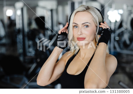 Athletic woman wearing headphones and gloves listening to music at the gym 131380005