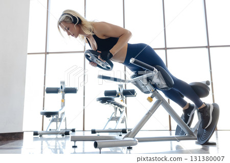Athletic woman performing back extension exercise using hyperextension bench in gym Athletic woman performing back extension exercise using hyperextension bench in gym 131380007