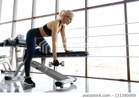 Athletic woman lifting dumbbell during workout in gym 131380009