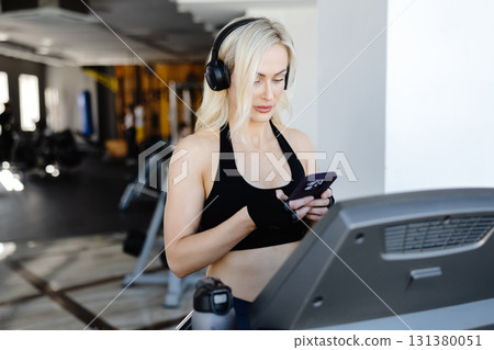 Athletic woman using smartphone and wearing headphones on treadmill in gym Athletic woman using smartphone and wearing headphones on treadmill in gym 131380051