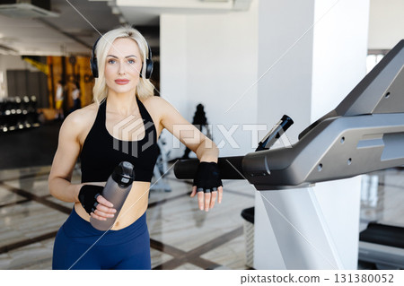 Athletic woman listening to music and drinking water in the gym 131380052