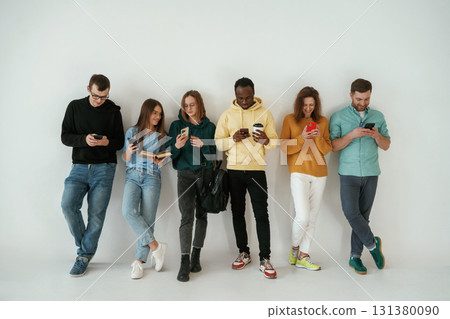With smartphones in hands. Group of young people are standing against white background With smartphones in hands. Group of young people are standing against white background 131380090