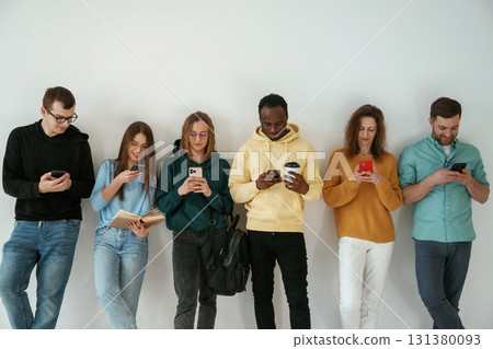 With smartphones in hands. Group of young people are standing against white background 131380093