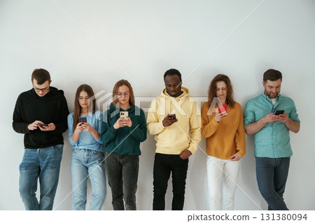 Busy by using smartphones. Group of young people are standing against white background 131380094