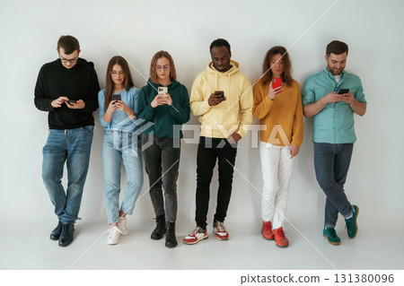 Busy by using smartphones. Group of young people are standing against white background 131380096