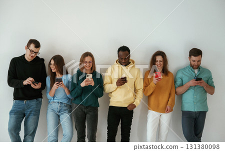 Joyful, holding smartphones. Group of young people are standing against white background 131380098