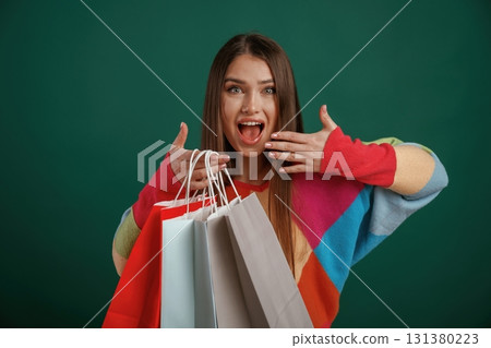 Crazy sale, shocked face, with shopping bags. Young woman is standing against green background in the studio Crazy sale, shocked face, with shopping bags. Young woman is standing against green background in the studio 131380223