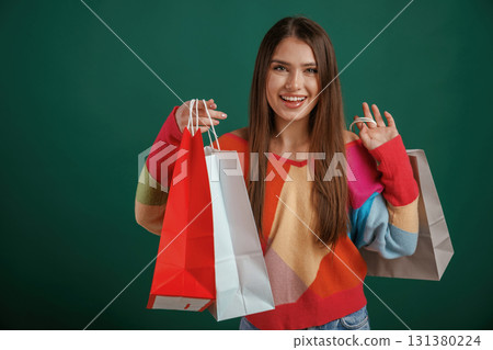 Conception of shopping, with bags. Young woman is standing against green background in the studio Conception of shopping, with bags. Young woman is standing against green background in the studio 131380224