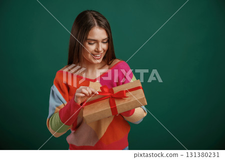 Holidays time. Holding gift box. Young woman is standing against green background in the studio 131380231