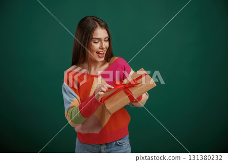Holidays time. Holding gift box. Young woman is standing against green background in the studio 131380232
