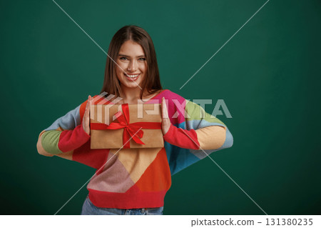 Holidays time. Holding gift box. Young woman is standing against green background in the studio Holidays time. Holding gift box. Young woman is standing against green background in the studio 131380235