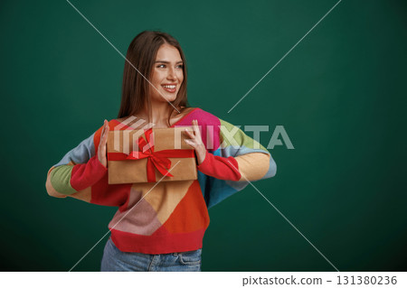 Holidays time. Holding gift box. Young woman is standing against green background in the studio Holidays time. Holding gift box. Young woman is standing against green background in the studio 131380236