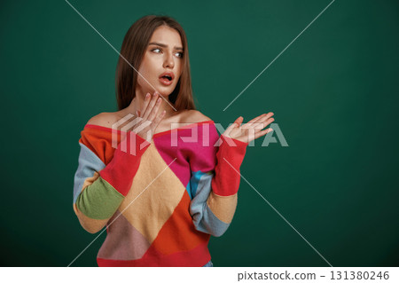 Thoughtful facial expression. Young woman is standing against green background in the studio Thoughtful facial expression. Young woman is standing against green background in the studio 131380246