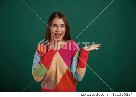 Showing by hand to the side, place for text. Young woman is standing against green background in the studio Showing by hand to the side, place for text. Young woman is standing against green background in the studio 131380254