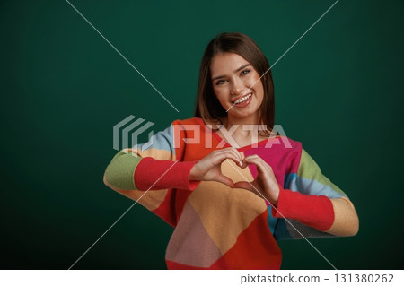 Heart shaped gesture by hands, sending love. Young woman is standing against green background in the studio Heart shaped gesture by hands, sending love. Young woman is standing against green background in the studio 131380262
