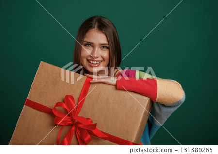 Large gift box in hands. Young woman is standing against green background in the studio Large gift box in hands. Young woman is standing against green background in the studio 131380265
