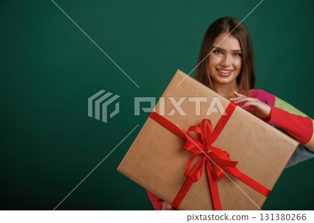 Large gift box in hands. Young woman is standing against green background in the studio 131380266