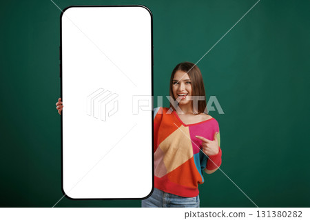 Large smartphone. White display for text or design. Young woman is standing against green background in the studio Large smartphone. White display for text or design. Young woman is standing against green background in the studio 131380282