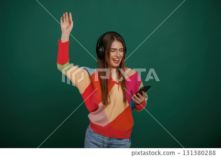 Feel the rhythm, listening to the music. Young woman is standing against green background in the studio Feel the rhythm, listening to the music. Young woman is standing against green background in the studio 131380288