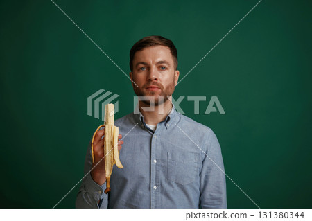 Holding banana. Man is standing against background in the studio 131380344