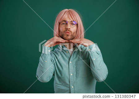 In glasses, posing, having fun. Gay man with pink hair is standing against green background 131380347
