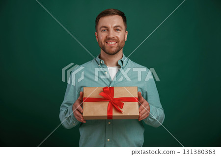 Little gift box in hands. Man is standing against background in the studio Little gift box in hands. Man is standing against background in the studio 131380363
