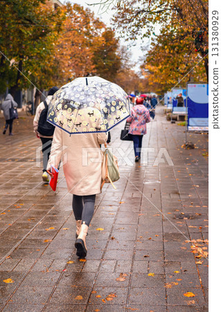 Woman walking down rainy autumn street with transparent umbrella. Concept of rainy day, street lifestyle, autumn, umbrella mood, rainy weather Woman walking down rainy autumn street with transparent umbrella. Concept of rainy day, street lifestyle, autumn, umbrella mood, rainy weather 131380929
