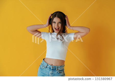 In headphones, enjoying music. Young woman is against yellow background In headphones, enjoying music. Young woman is against yellow background 131380967
