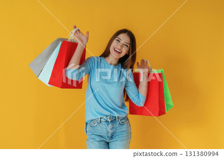 Colorful shopping bags in hands. Young woman is against yellow background 131380994