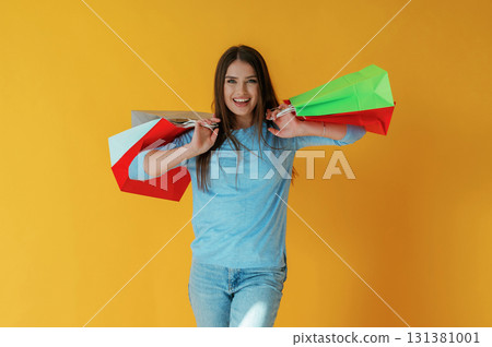 Standing and holding shopping bags. Young woman is against yellow background 131381001