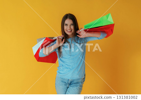 Standing and holding shopping bags. Young woman is against yellow background 131381002