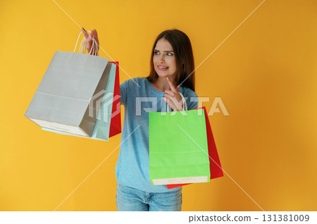 Young woman is against yellow background. Holding shopping bags Young woman is against yellow background. Holding shopping bags 131381009