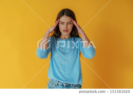 Bad headache. Young woman is against yellow background Bad headache. Young woman is against yellow background 131381020