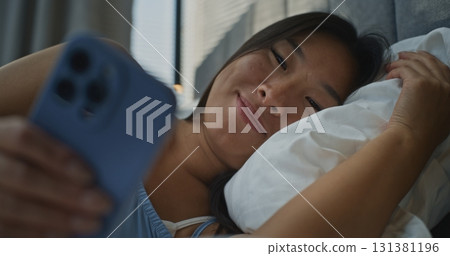 Young Woman Feels Positive Emotions as Chats Online While Lying In Bed 131381196