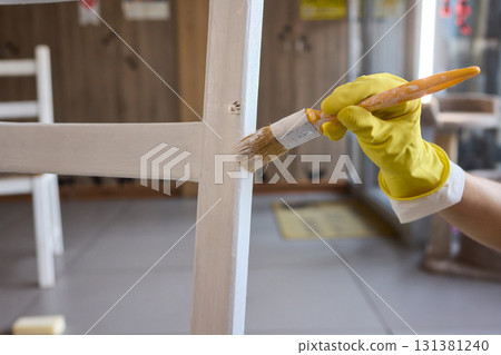 Engage in DIY chair restoration using a paint brush and protective gloves for the process 131381240