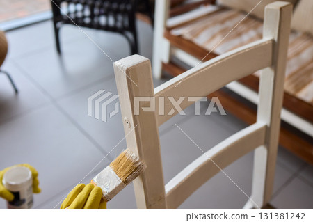 Engage in DIY chair restoration using a paint brush and protective gloves for the process 131381242