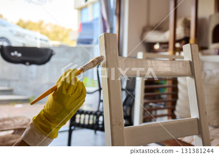 Engage in DIY chair restoration using a paint brush and protective gloves for the process 131381244